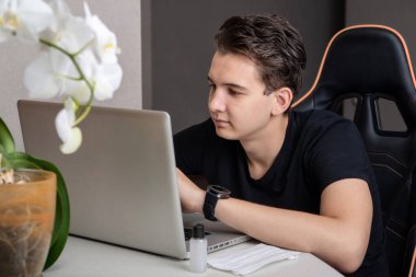 Siyah tişörtlü yakışıklı genç adam dizüstü bilgisayarda çalışıyor ve gülümsüyor. İş adamı masada otururken kameraya bakıyor ve merkez ofisteki dizüstü bilgisayarda çalışıyor..