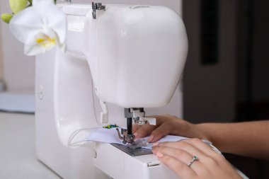 Koronavirüs pandemisi sırasında dikiş makinesini kullanarak tıbbi maske takan bir kadın. Covid 19 virüsüne karşı ev yapımı koruyucu maske..