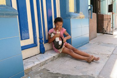 Küba, Havana - 07 Nisan, 2016: sıcak Küba güneşten gizleme gölgede, onu eve önünde yere oturmuş onu evde beslenen hayvan kedi ile oynarken küçük bir Küba kız