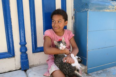 Küba, Havana - 07 Nisan, 2016: sıcak Küba güneşten gizleme gölgede, onu eve önünde yere oturmuş onu evde beslenen hayvan kedi ile oynarken küçük bir Küba kız