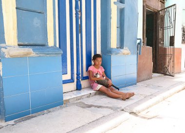 Küba, Havana - 07 Nisan, 2016: sıcak Küba güneşten gizleme gölgede, onu eve önünde yere oturmuş onu evde beslenen hayvan kedi ile oynarken küçük bir Küba kız