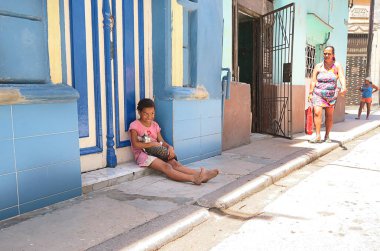 Küba, Havana - 07 Nisan, 2016: sıcak Küba güneşten gizleme gölgede, onu eve önünde yere oturmuş onu evde beslenen hayvan kedi ile oynarken küçük bir gülümseyen Küba kız