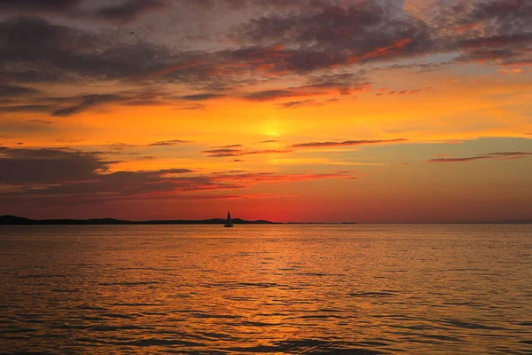 amazing meditation sunset on the Adriatic Sea, still water, light breeze, perfect atmosphere to contemplate on life, red and orange hue of the sky with orange reflaction as a path in the sea, and a little sail boat floating
