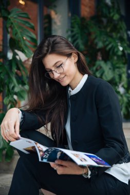 Genç güzel esmer kız, ofis giyim tarzı, bir kafede bir masada sokakta oturan, sokak modeli poz tarzı, bir not defterinotlar yapar, telefonda konuşurken