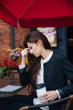 Genç güzel esmer kız, ofis giyim tarzı, bir kafede bir masada sokakta oturan, sokak modeli poz tarzı, bir not defterinotlar yapar, telefonda konuşurken