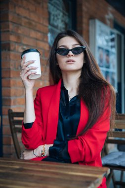 Genç güzel esmer kız, ofis giyim tarzı, bir kafede bir masada sokakta oturan, sokak modeli poz tarzı, bir not defterinotlar yapar, telefonda konuşurken