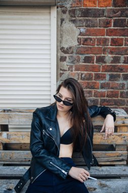 deri ceketli genç kız sigara içiyor, rock tarzı, arsız ve sevimli kız sokak poz tarzı, rock punk yaşam tarzı