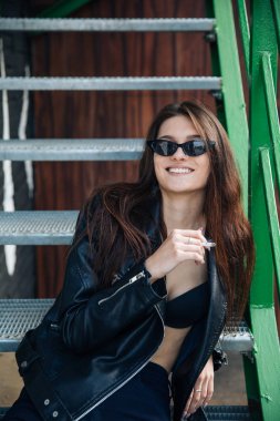 deri ceketli genç kız sigara içiyor, rock tarzı, arsız ve sevimli kız sokak poz tarzı, rock punk yaşam tarzı