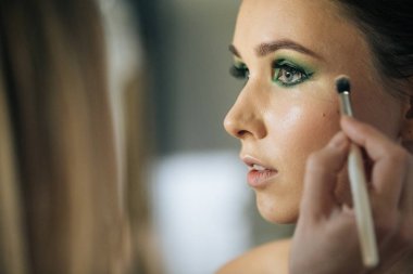 Profesyonel makyöz, fırça ve diğer yöntemlerle makyaj yapar, güzel bir genç kızın yüzüne harika makyaj yapar, güzellik makyajı yapar, yüzüne yağ sürer ve kırmızı renk önceliği ile parlar.