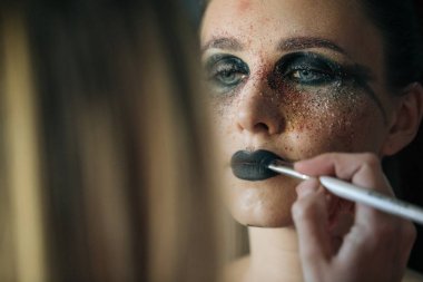 Profesyonel makyöz, fırça ve diğer yöntemlerle makyaj yapar, güzel bir genç kızın yüzüne harika makyaj yapar, güzellik makyajı yapar, yüzüne yağ sürer ve kırmızı renk önceliği ile parlar.