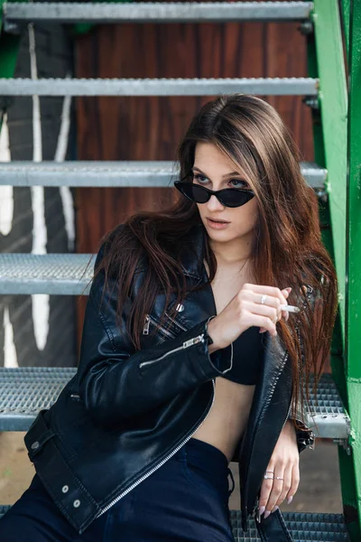 Young Girl In A Leather Jacket Smokes Cigarettes Rock Style Cheeky And Cute Girl Street Posing Style Rock Punk Lifestyle Black Attractive Stock Photo Young Girl In A Leather Jacket Smokes Cigarettes Rock Style Cheeky And Cute Girl Street Posing Style Rock Punk Lifestyle Black Attractive Stock Photo