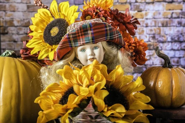孩子的娃娃与长的金发蓝色玻璃眼睛和红色帽子围拢橙色南瓜黄色向日葵和秋天花花束 — 图库照片