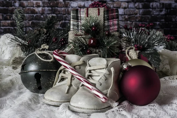 baby shoes on white with green Christmas bell red and green ornaments and canndy cane with brick wall background and presents