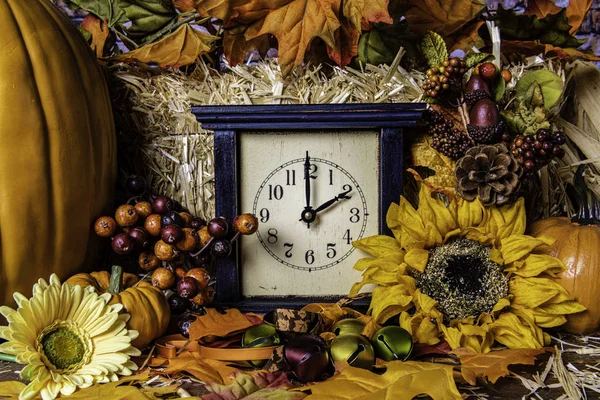 fall scene with old wooden clock set back to standard for fall surrounded by yellow sunflowers orange pumpkins autumn leaves and bale of straw background