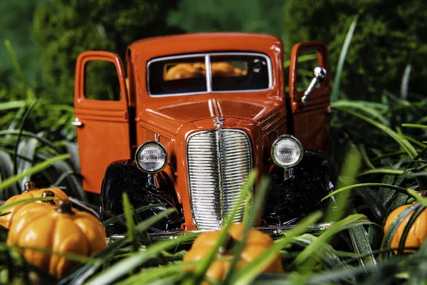 fall scene with old red toy pick up truck filled with orange pumpkins in pumpkin patch for Halloween with tall green grass and green background