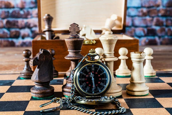 still life gold pocket watch and chain isolated on chess board with wood chess pieces and box on wood table