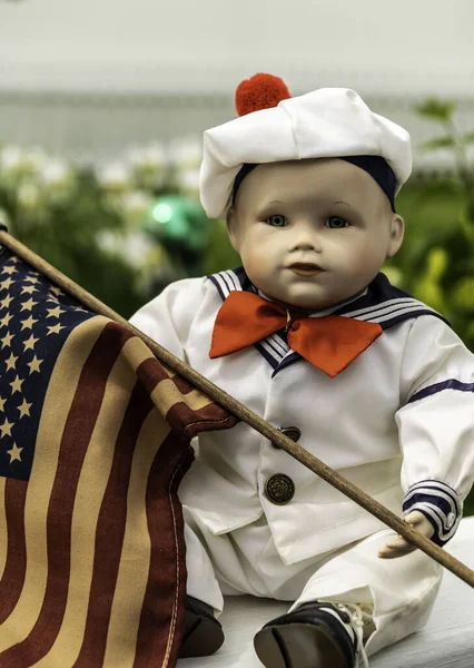 vintage small boy doll with glass eyes dressed in sailor costume vertical format outdoors holding american flag