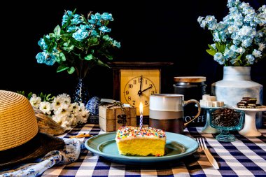 Doğum günü pastası yanan mum ve gökkuşağı üzerine çiçekler ve kahve serpiştirilmiş.