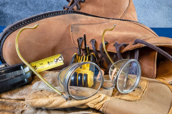 带黄色带尺寸的皮制工作手套的旧安全玻璃和带蓝色底皮制工作靴的各种钥匙 — 图库照片