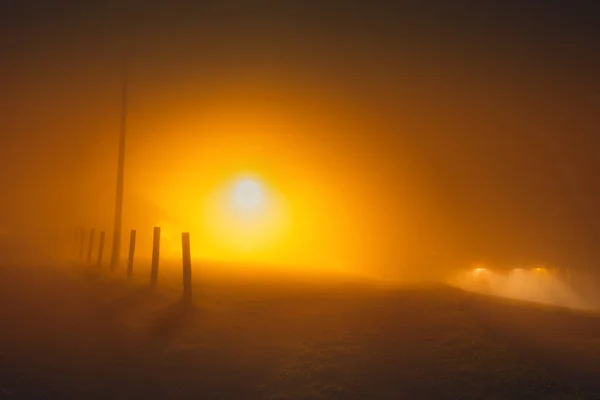 Foggy countryside street at night in the orange light of a street lamp
