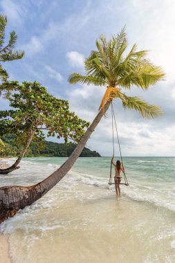 Genç seksi kız bikini bir salıncak bir egzotik tropik kum plajındaki Bai Sao denizin altında bir palmiye ağacı üzerinde