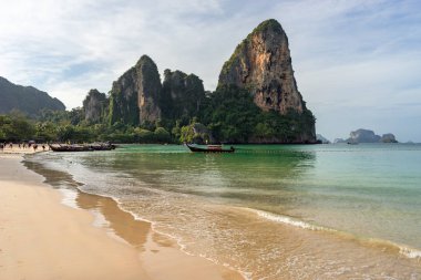 Kumlu plajın, berrak denizin, kıyı şeridinin, kayaların ve teknelerin sabahları sudaki manzaraları