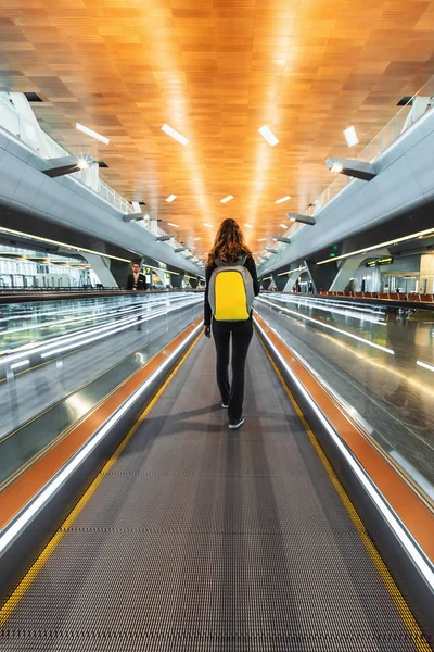 One woman traveller with backpack go on moving walkway travolator in new Hamad International Airport. Back view