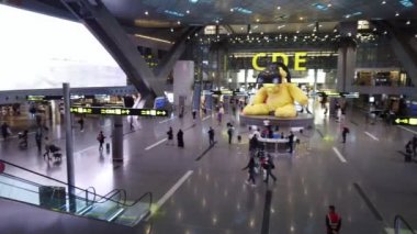 Doha, Katar - 11 Ocak 2019: Hamad uluslararası havaalanı terminali büyük sarı ayıile. Hareket eden insanlar da yüksek açı görünümü. Kamera kaydırışları soldan sağa 