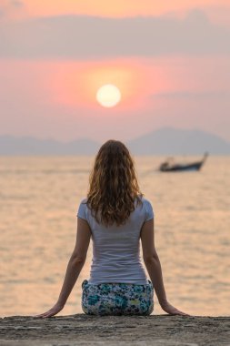 Genç bir kadın deniz kıyısında tek başına oturur ve güzel gün batımına bakar