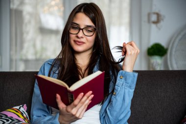 Evdeki kanepede oturup kitap okuyan rahat, mutlu bir kadın..