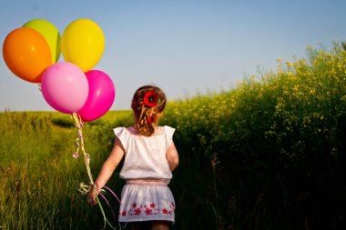 yeşil buğday alanıyla aracılığıyla çalışan elbiseli küçük Asya kız elinde, ağır çekim balonlar