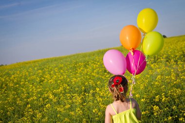 Güzel kıyafet elinde balonlarla günbatımında altın buğday alanında çalışan, küçük kız. Arkadan görüntülemek