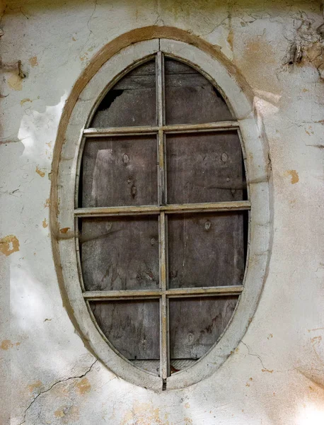 An old oval window is installed in a stone wall.