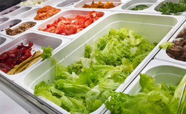aşçı, bir kase salata sebze parçaları koyar. Penceredeki bir fast food restoran salata için tepsi ile karışık