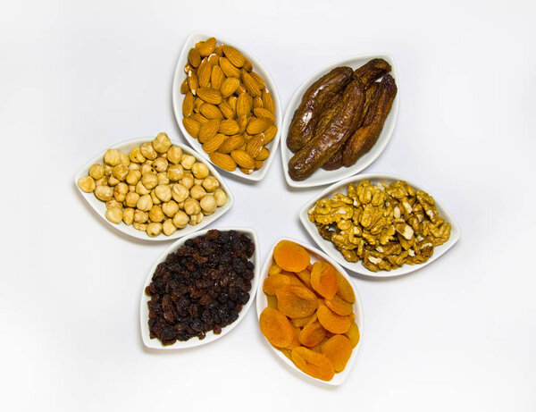 The assortment of nuts and dried fruits in bowls on a white background is a top view.
