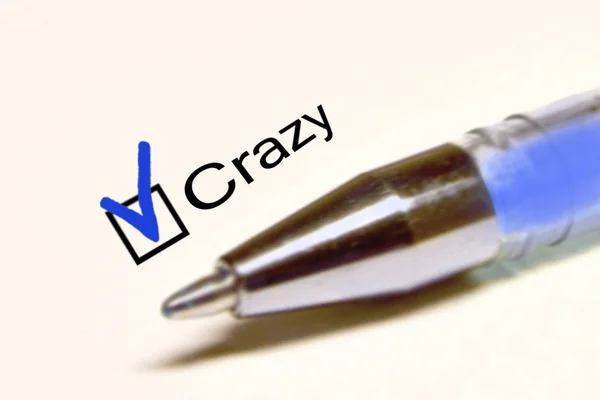 Penna blu e la scritta CRAZY con croce sulla carta bianca — Foto Stock