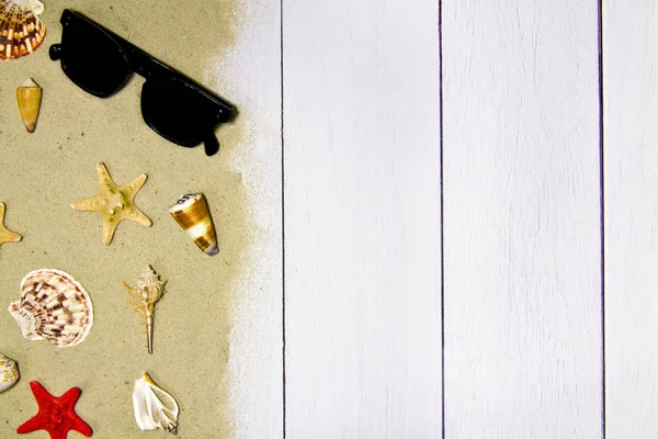 Conchiglie, stelle, occhiali da sole su uno sfondo di legno chiaro con sabbia, vista dall'alto — Foto Stock