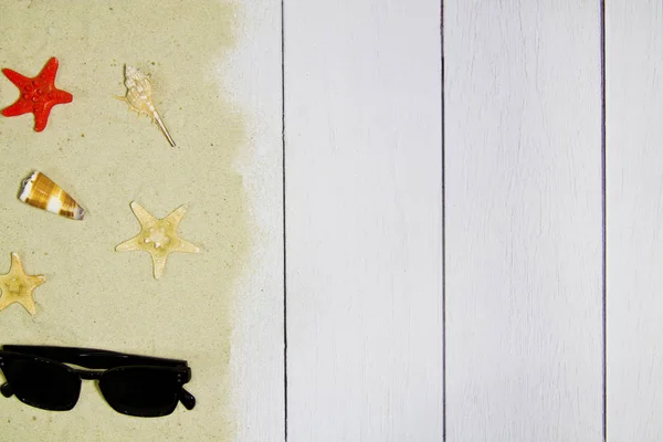 Морські раковини, зірки, сонцезахисні окуляри на світлому дерев'яному фоні з піском, вид зверху — стокове фото
