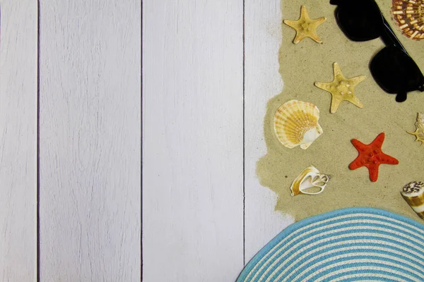 Морські раковини, зірки, сонцезахисні окуляри, капелюх на світлому дерев'яному фоні з піском, вид зверху — стокове фото
