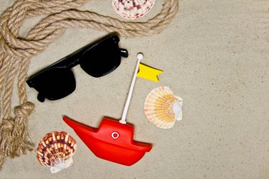 Kırmızı oyuncak gemi ile kum arka plan üzerinde deniz kabukları ve deniz ipdekorasyonu