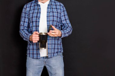 Siyah arka plandaki bir adamın elinde siyah termo bardak..