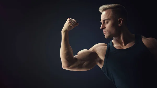 Ung instängd muskelbyggaren killen visar biceps på svart rygg — Stockfoto