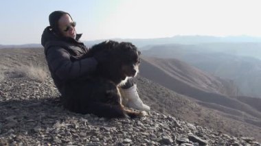 Turist kış giysileri bir kızı bir kanyon bakan bir dağ kenarında oturur ve aktif bir köpek vuruş