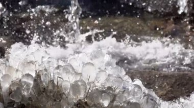 Bir kayaya hızlı dağ nehir ortasında donmuş su. Ağır çekim 240 fps hızında
