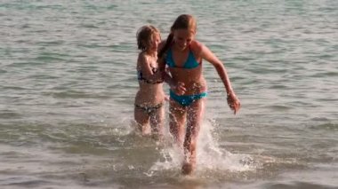 Sudaki Yaz Oyunları. İki genç kız aktif ve neşeli bir şekilde sudan karaya çıkıp bir sürü sıçrama yaratıyor.