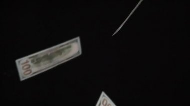 Nakit akışı. Döngü. Parasal değerler 100 dolar ve yavaşça siyah arkaplan üzerine düşüyor. 240 fps hızla çekiliyor.