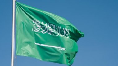 Suudi Arabistan bayrağı rüzgarı dalgalandırıyor. Büyük Eyalet Bayrağı güneş tarafından aydınlatılır ve mavi gökyüzüne karşı destansı bir şekilde dalgalanır. Slow Motion 240 fps