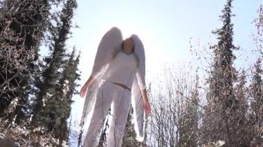 Orman Ormanı 'ndaki Beyaz Giyen Melek. Arka plandaki güzel kız kollarını gökyüzüne kaldırıyor. Arkasında beyaz kanatları var. Havada beyaz tüyler uçuşuyor. Slow Motion 240 fps hızında