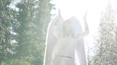Beyazlı Melek, Güneş Işığıyla yıkandı. Arka plandaki güzel kız kollarını gökyüzüne kaldırıyor. Arkasında beyaz kanatları var. Havada beyaz tüyler uçuşuyor. Slow Motion 240 fps hızında