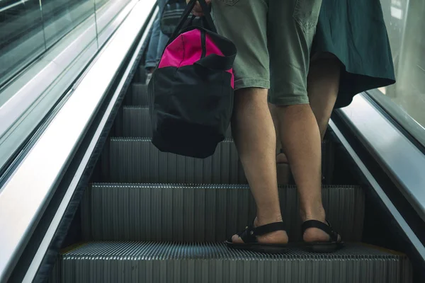 a man with a bag on a trip is understood on the escalator. a man holding a pink bag and riding an escalator. man collected things and flies off on leave at the airport